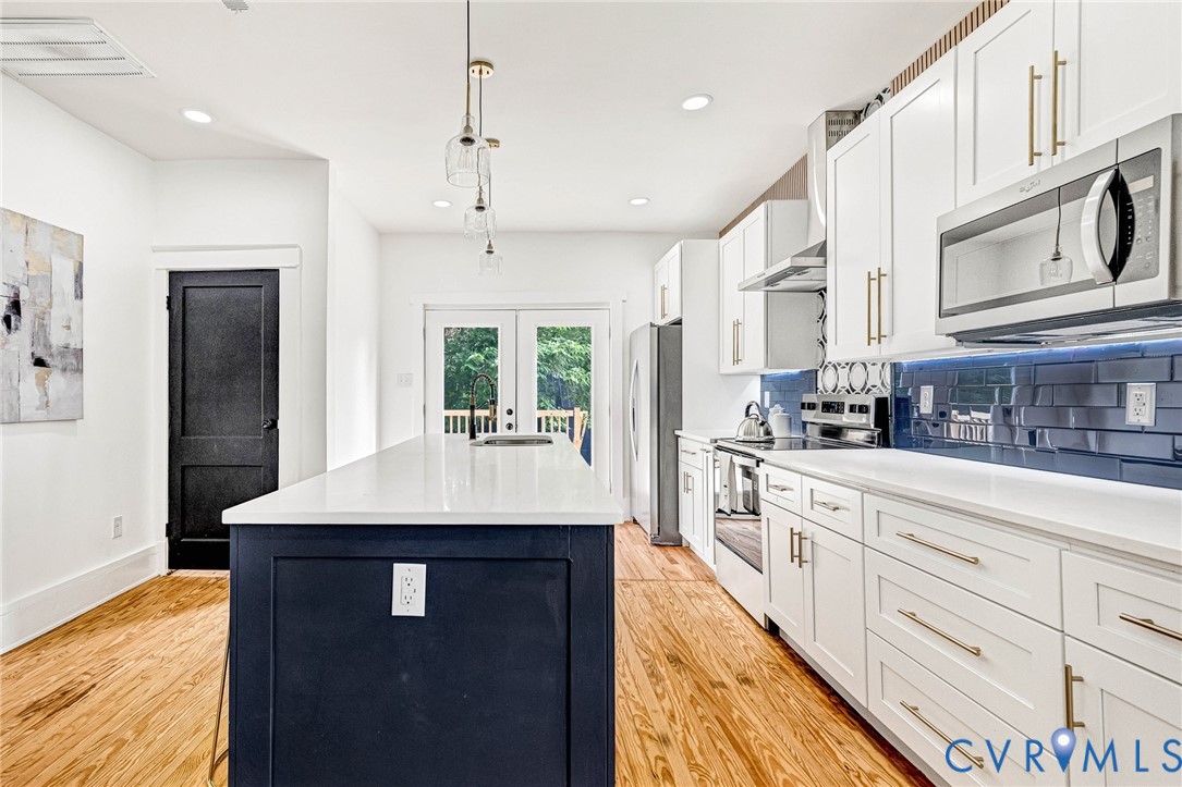 Modern kitchen featuring white cabinetry, a blue subway tile backsplash, stainless steel appliances, a center island with a white countertop, and wood-finish flooring