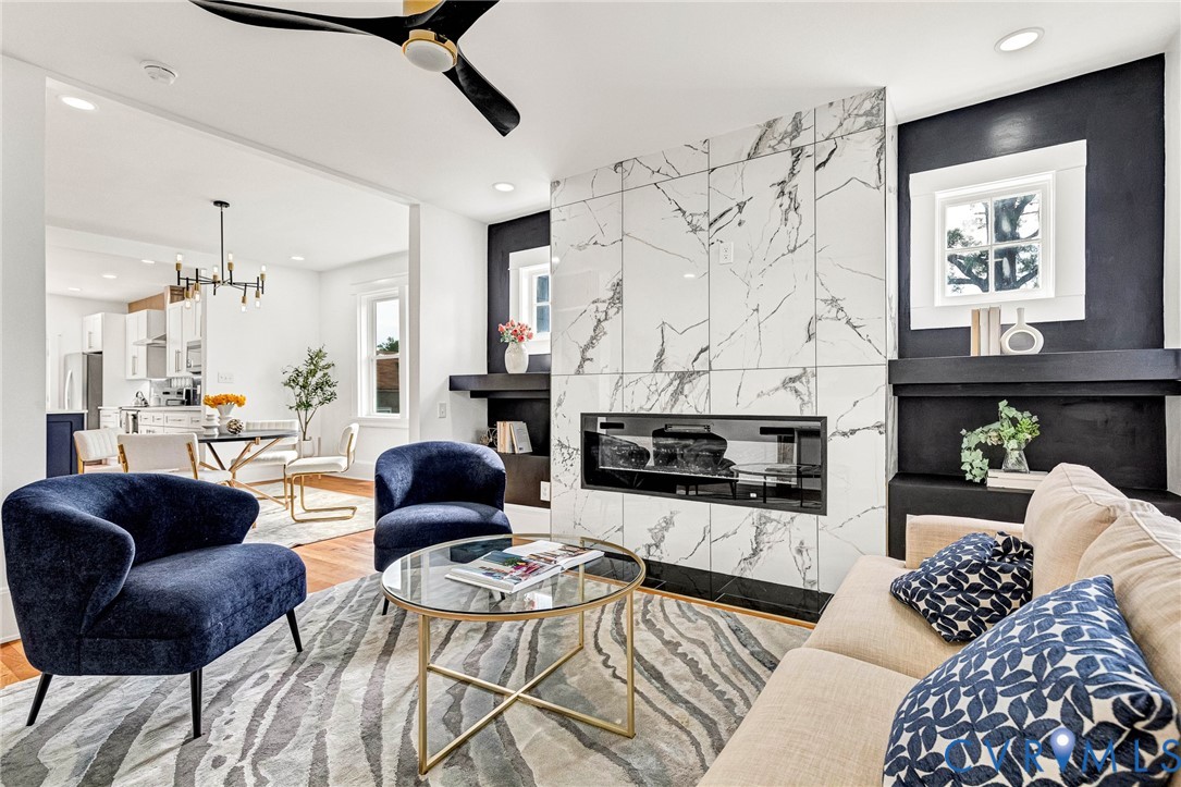 Modern linear fireplace with a stone-look surround, wood-finish flooring, and a contemporary ceiling fan