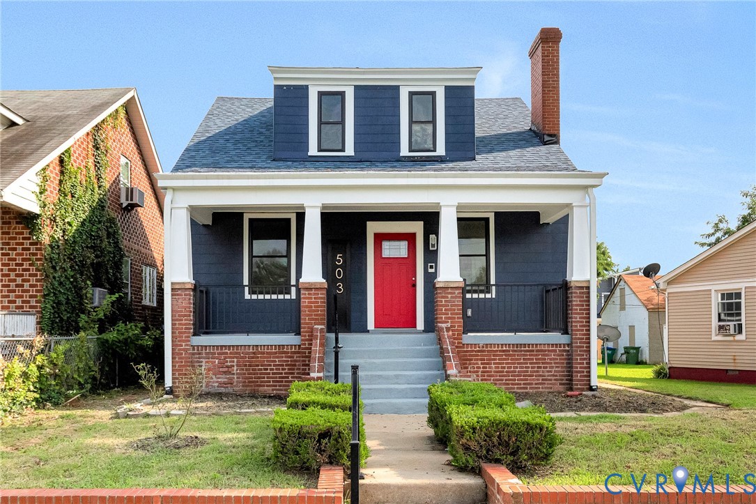 Exterior featuring a prominent red entry door, white columned porch, brick foundation, and dark siding with white trim