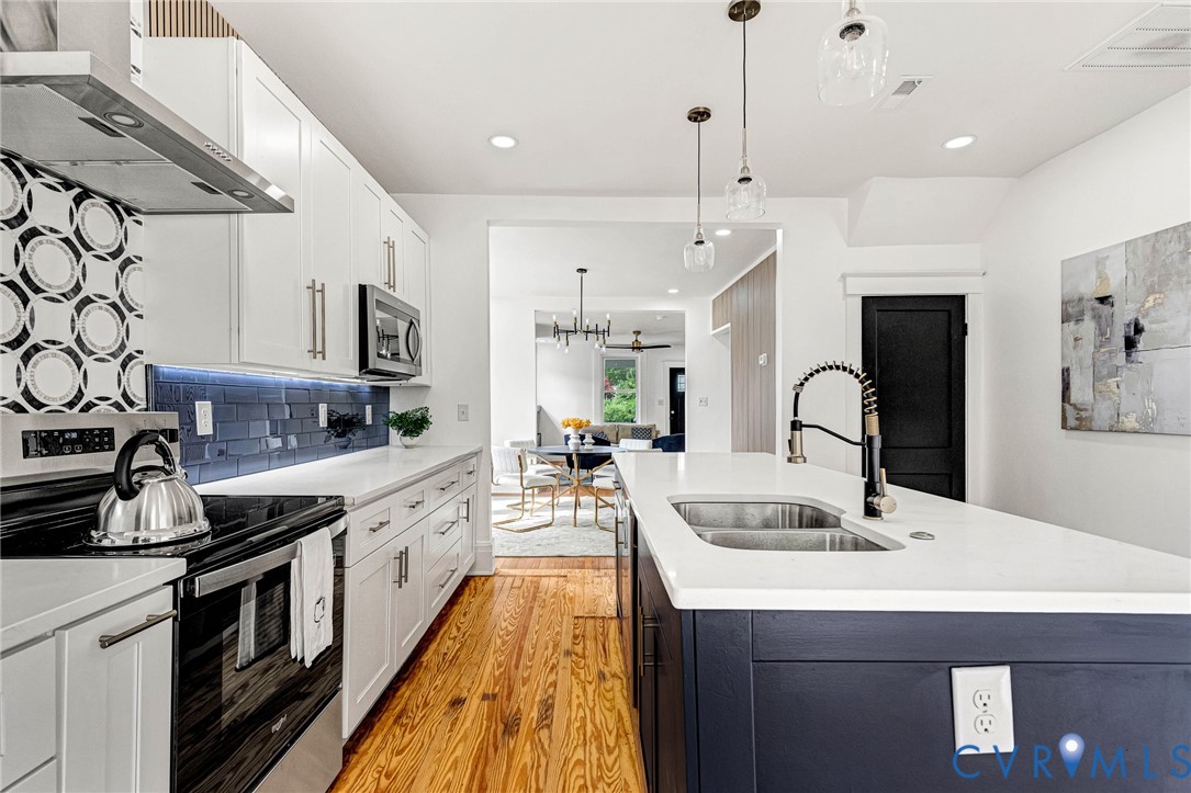 Kitchen featuring an island with double basin sink, white countertops, wood-finish flooring, and white cabinetry with stainless steel appliances