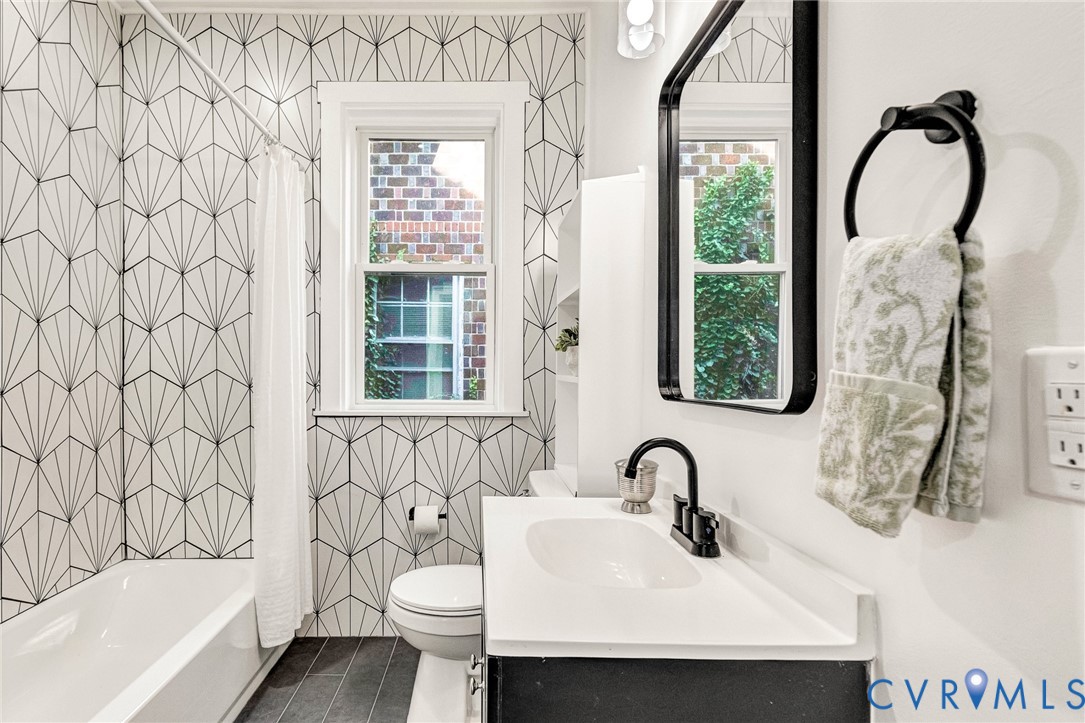 Bathroom featuring a white bathtub, a single vanity with a white countertop and dark cabinet, a black-framed mirror, and geometric pattern wall tile