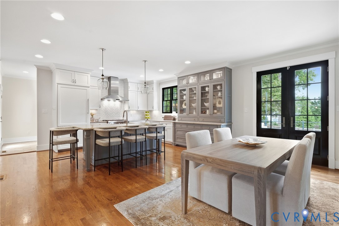 Hardwood flooring throughout, kitchen island with seating, stainless steel appliances, built-in display cabinetry, and black-framed French doors