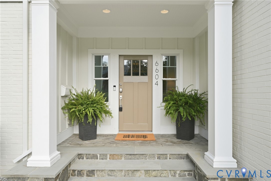 Covered entryway featuring a paneled door with glass inserts, transom window, and flanking sidelight windows Covered entryway featuring a paneled door with glass inserts, transom window, and flanking sidelight windows