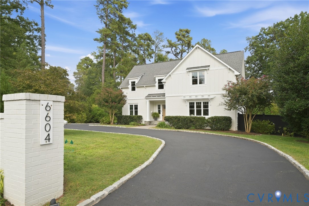 White brick facade, prominent gable roof, asphalt driveway with stone curbing, brick address monument, and established landscaping