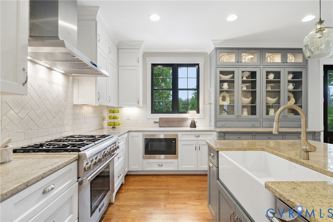 Gourmet kitchen featuring a large range with stainless steel hood, built-in microwave, white shaker cabinetry, a farmhouse sink, and grey built-in display cabinetry Gourmet kitchen featuring a large range with stainless steel hood, built-in microwave, white shaker cabinetry, a farmhouse sink, and grey built-in display cabinetry