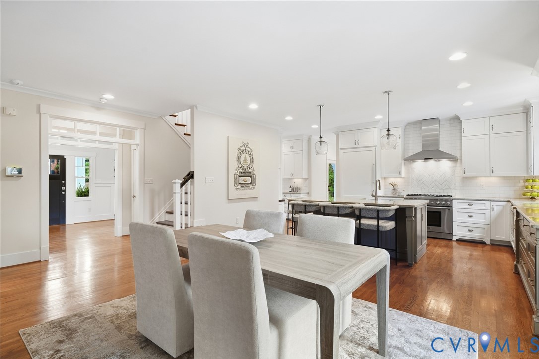 Hardwood flooring throughout, white shaker cabinetry, stainless steel appliances, kitchen island with counter seating, and recessed lighting