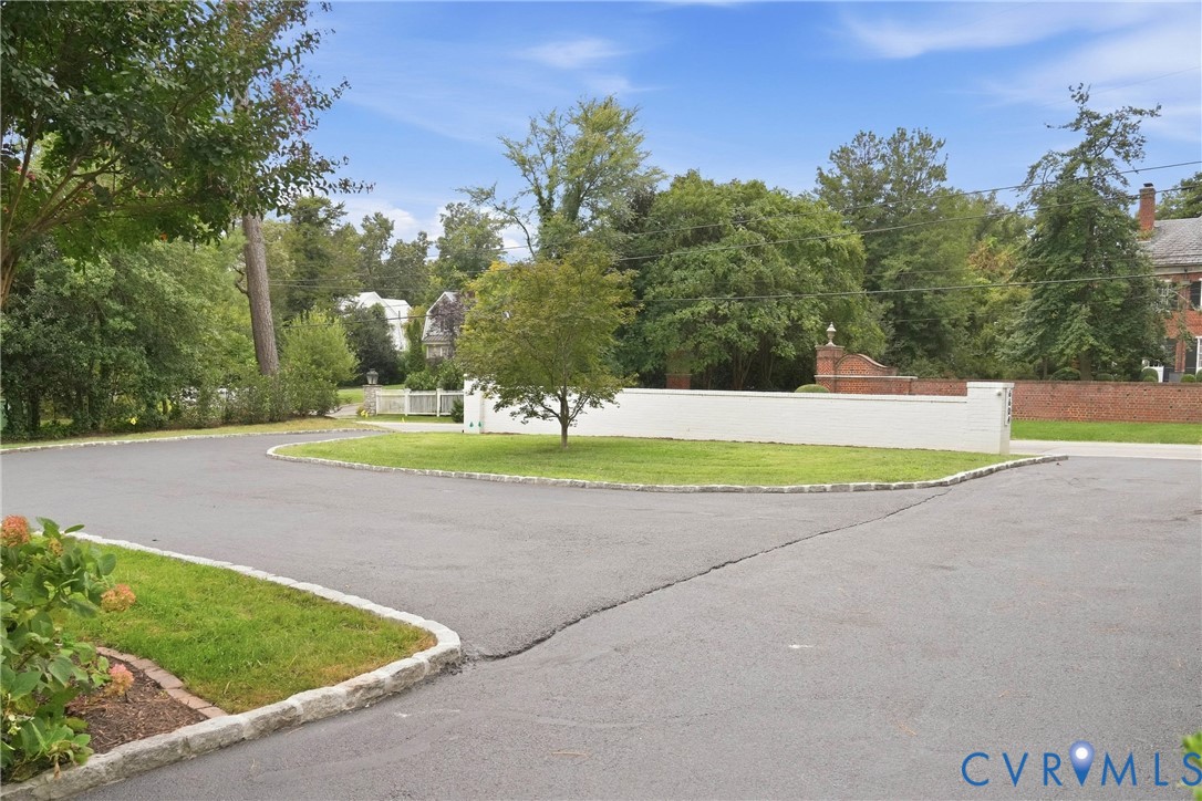 Paved asphalt driveway with stone curbing, flanked by a manicured lawn and mature trees