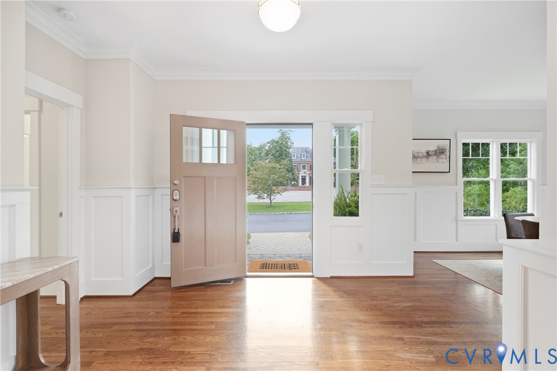 Hardwood flooring, wainscoting, crown molding, transom window, and paneled entry door Hardwood flooring, wainscoting, crown molding, transom window, and paneled entry door