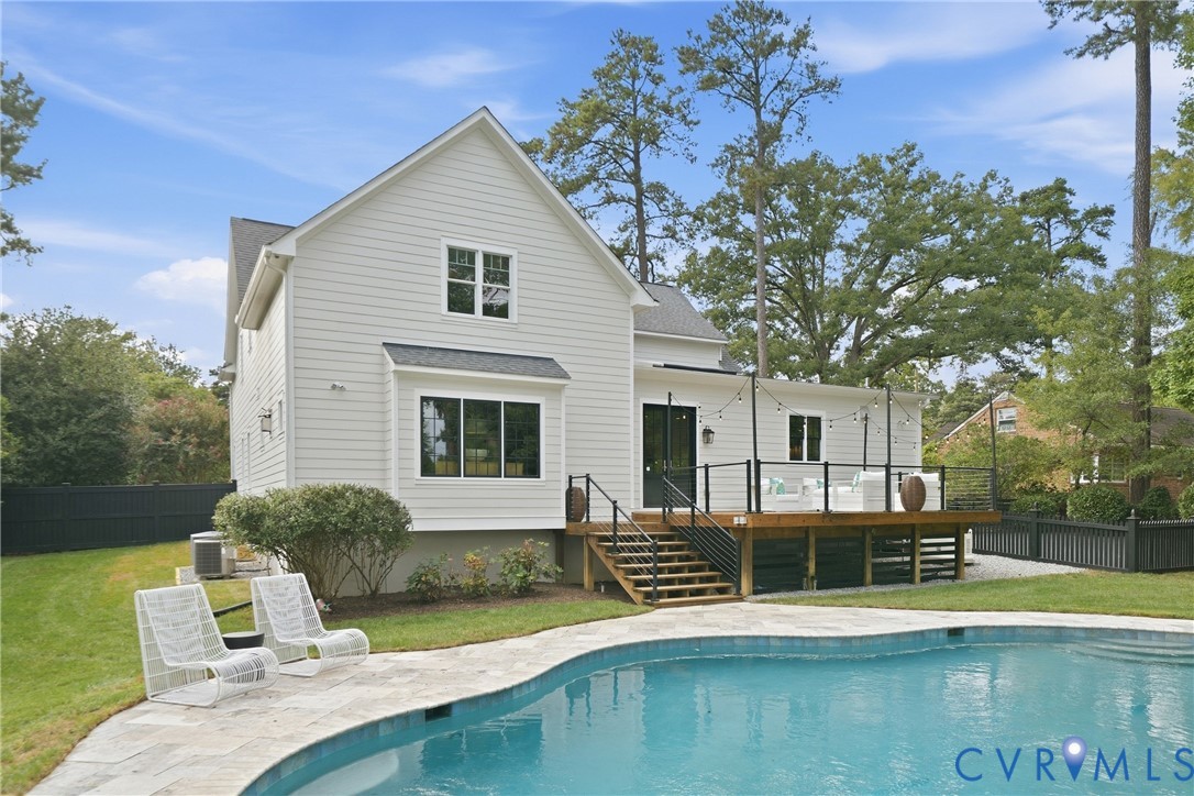 White siding exterior with a multi-level wood deck, black metal railing, and an in-ground swimming pool featuring a flagstone surround White siding exterior with a multi-level wood deck, black metal railing, and an in-ground swimming pool featuring a flagstone surround