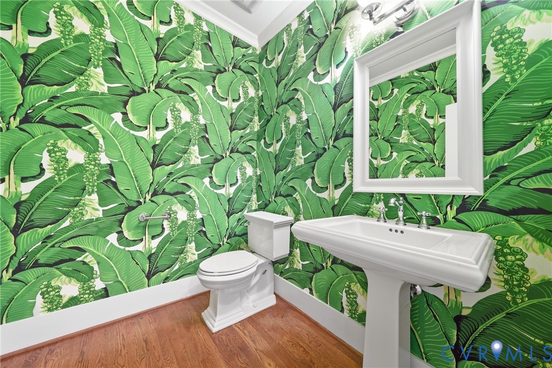 Hardwood-finish flooring, pedestal sink with chrome faucet, framed mirror, and crown molding