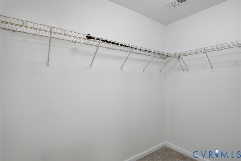 Wall-mounted wire shelving system, integrated hanging rod, light gray carpet, and white painted walls
