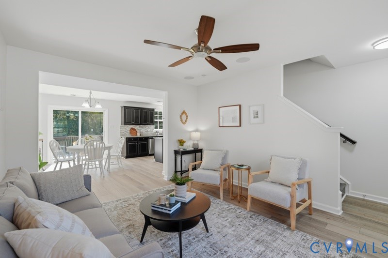 Bright living space featuring wood-finish flooring, a ceiling fan, and access to a kitchen with dark cabinetry and stainless steel appliances
