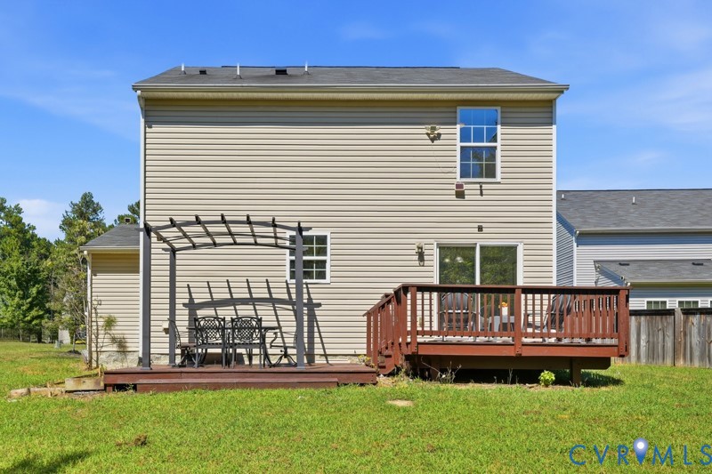 Exterior featuring tan siding, a brown wood-finish deck, a metal pergola, sliding glass doors, and a second-story window with grilles
