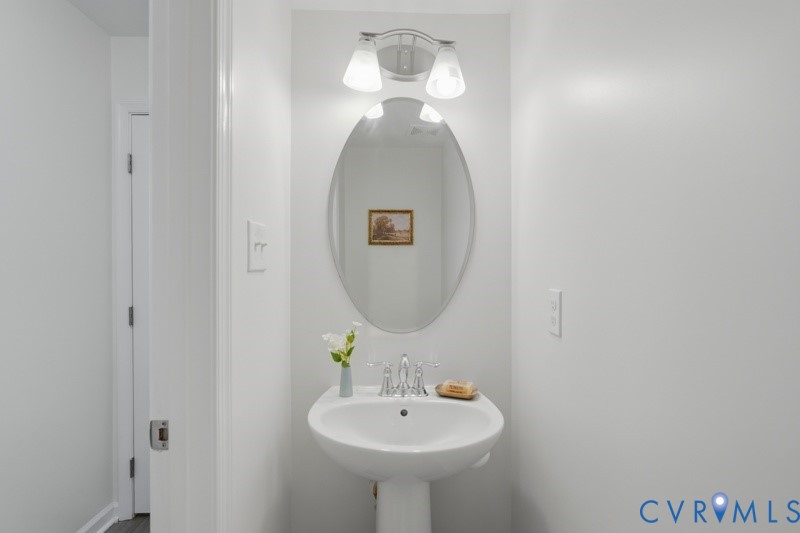 Pedestal sink with chrome faucet, oval mirror, and wall-mounted light fixture