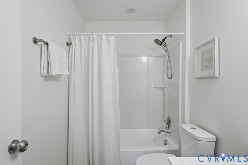 White bathtub and shower combination with a curved shower curtain rod, a chrome showerhead, and recessed ceiling lighting