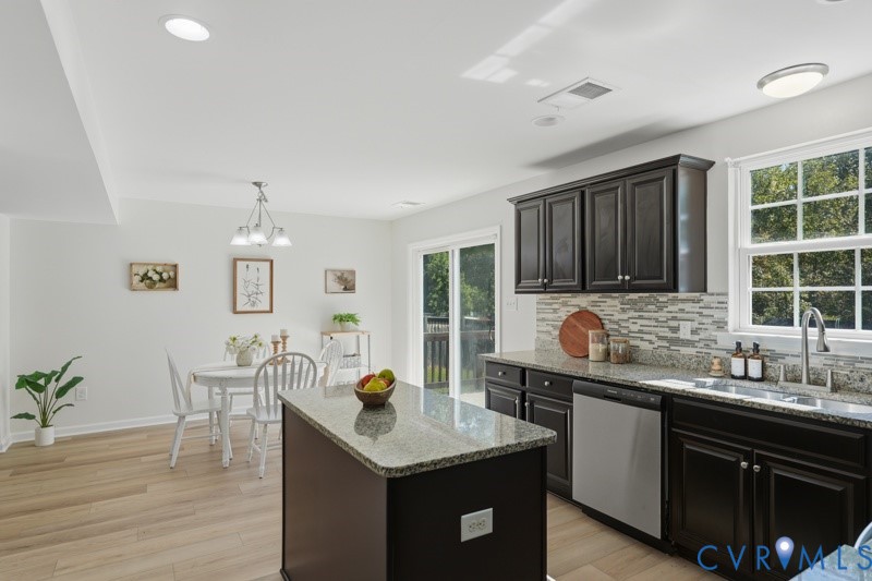 Kitchen featuring dark wood cabinetry, stainless steel dishwasher, an island with a light-colored countertop, and a tile backsplash