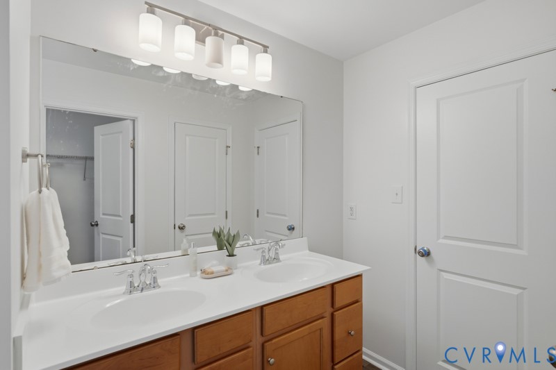 Double vanity with integrated sinks, wood-finish cabinetry, chrome faucets, and an expansive wall mirror