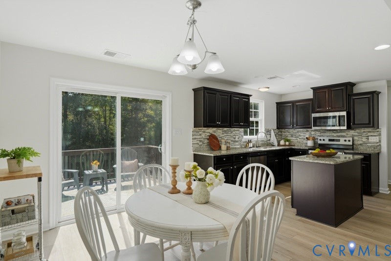 Kitchen featuring dark wood-finish cabinetry, a stone-finish backsplash, stainless steel appliances, and a central island with a stone-finish countertop