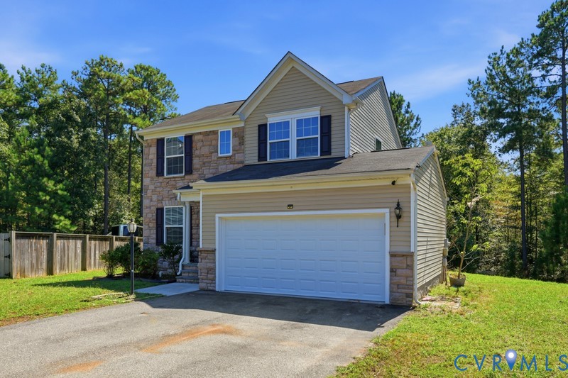 Stone facade accents, siding exterior, attached two-car garage, paved driveway, and a wood privacy fence