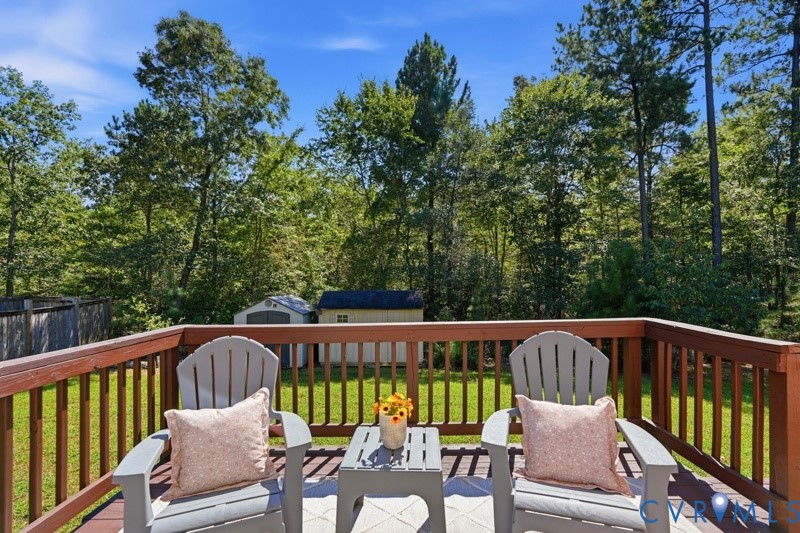 Expansive wood-finish deck with a wood railing, overlooking a fenced backyard with a storage shed and mature trees