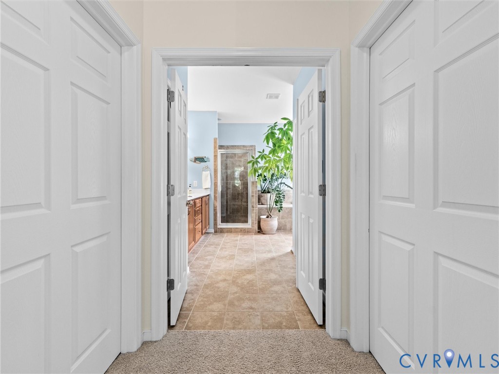Carpeted hallway with panel doors opening to a bathroom featuring a tile floor, wood-finish vanity, and glass-enclosed shower