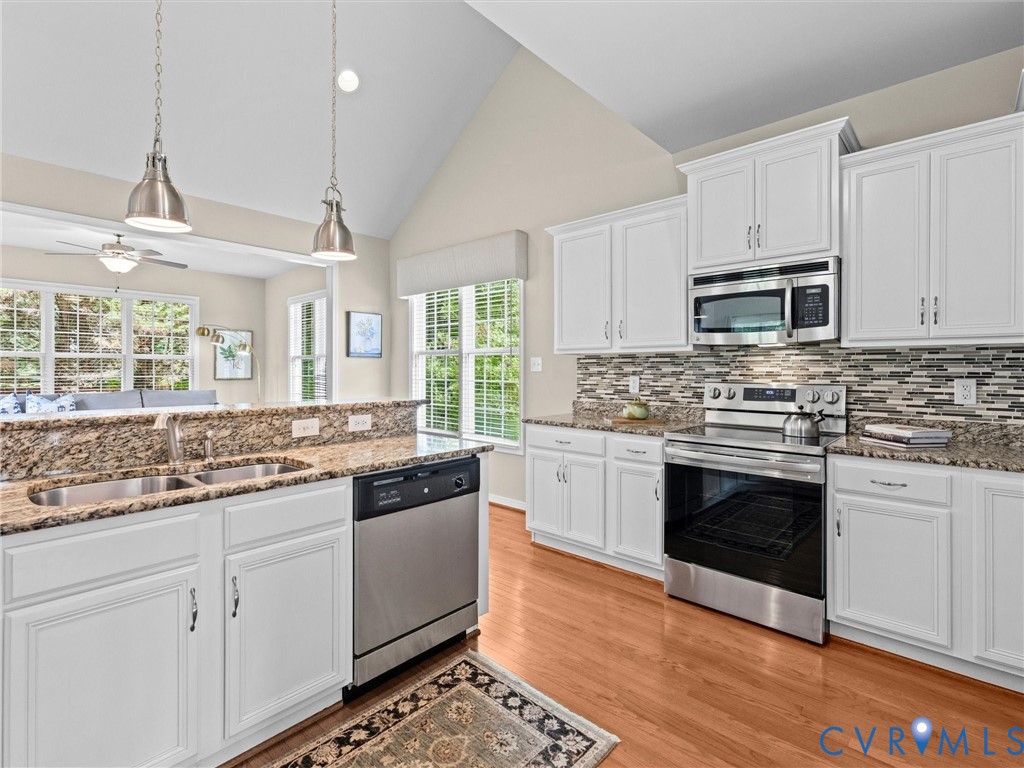 Kitchen featuring white cabinetry, stainless steel appliances, dual basin sink, granite countertops, and wood-finish flooring