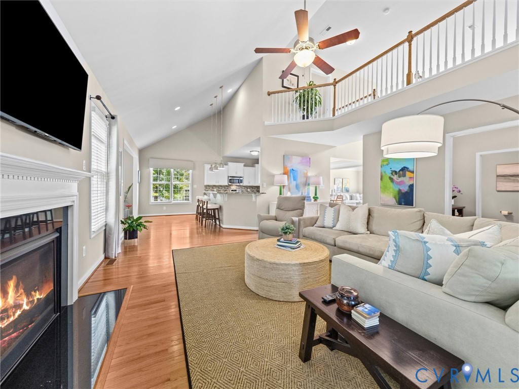 Vaulted ceiling featuring a ceiling fan, fireplace with a white mantel, hardwood flooring, and an open concept layout