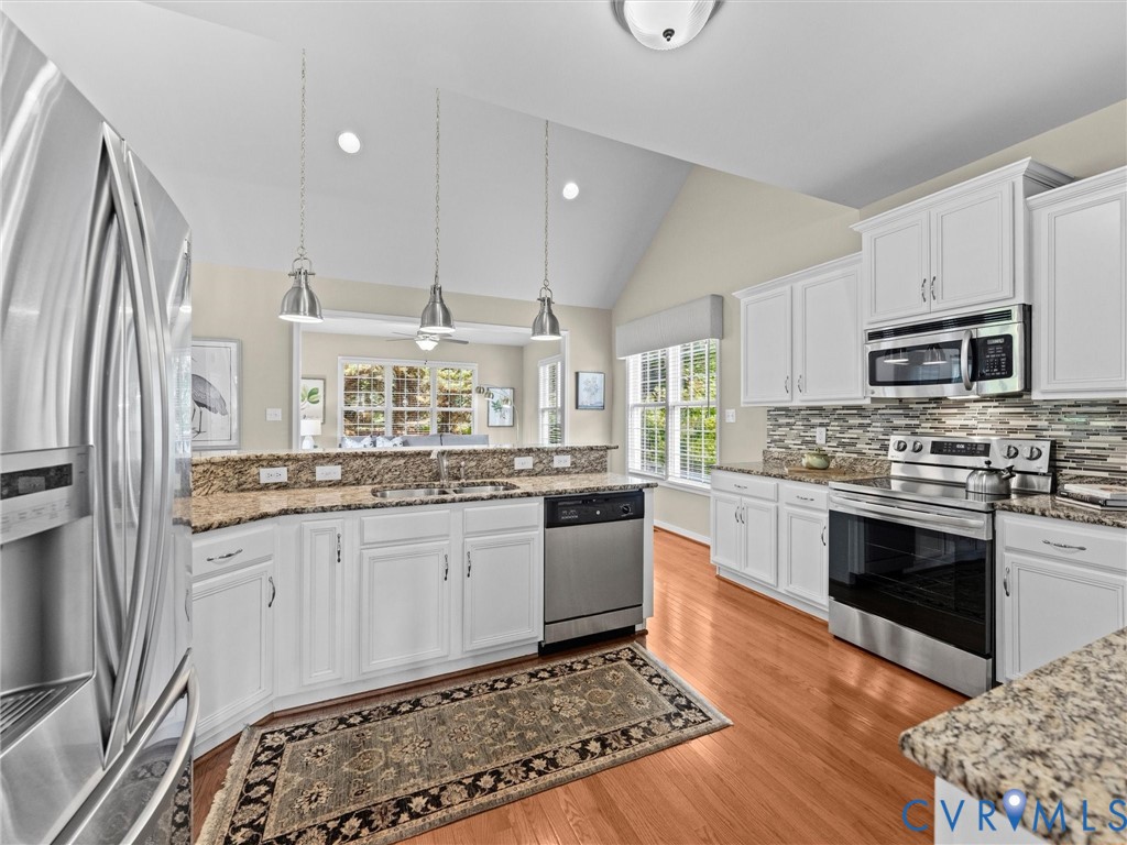 Vaulted ceiling with recessed lighting, white cabinetry, stainless steel appliances, granite countertops, and wood-finish flooring