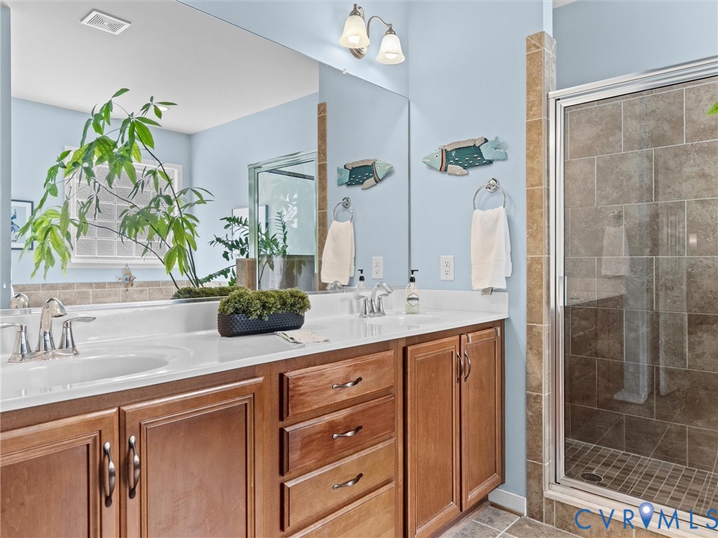 Double vanity with undermount sinks and wood cabinetry, large mirror, tile flooring, and glass-enclosed shower with tile surround