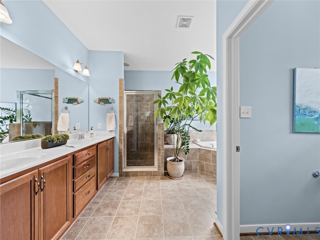 Double vanity with wood-finish cabinetry, a glass-enclosed shower, a built-in soaking tub, and tile flooring
