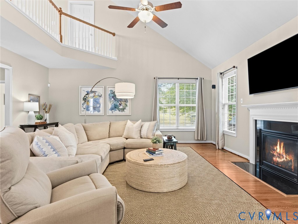 Vaulted ceiling with an overhead fan, hardwood flooring, fireplace with a mantel, and architectural railing