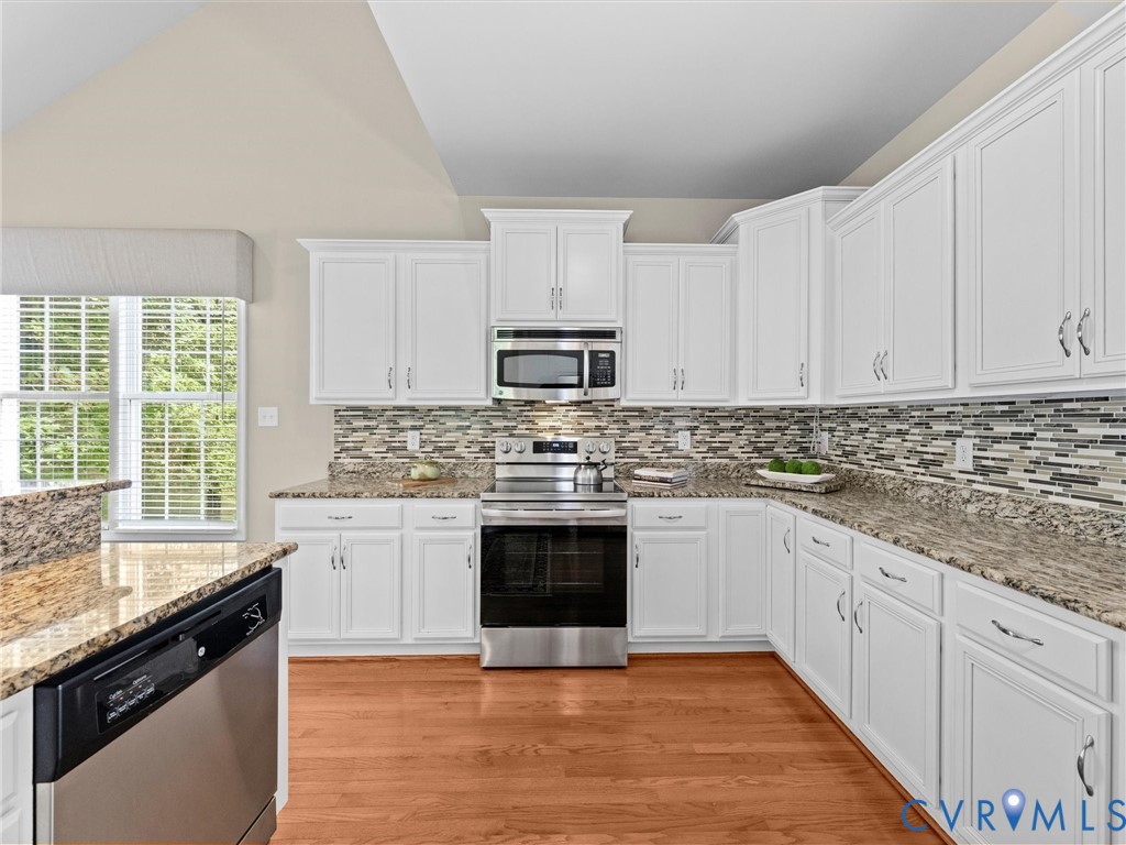 Kitchen featuring white cabinetry, granite countertops, tile backsplash, stainless steel appliances, and wood-finish flooring