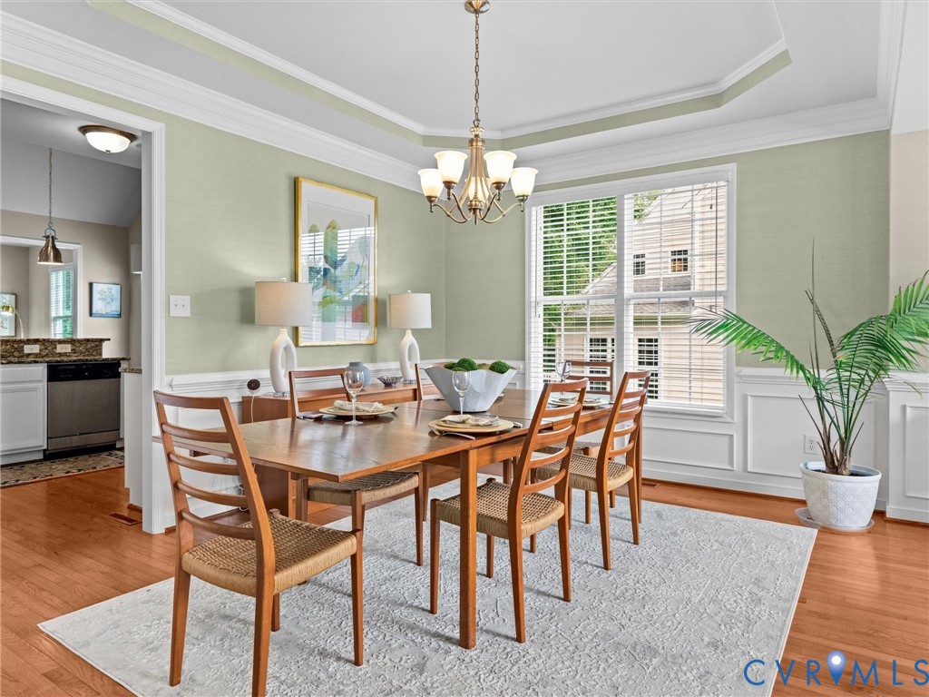 Tray ceiling with crown molding, wood-finish flooring, white paneled wainscoting, and large window