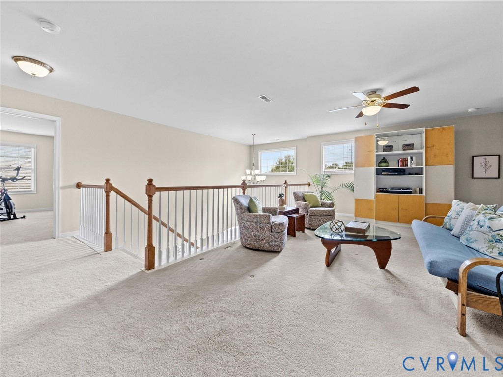 Carpeted loft area with multiple windows, a ceiling fan, and built-in shelving