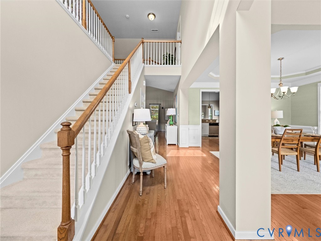 Two-story foyer with hardwood flooring, carpeted staircase with wood handrail, and white balusters