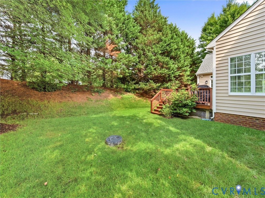 Expansive grassy yard with mature trees, wood deck, and wood siding