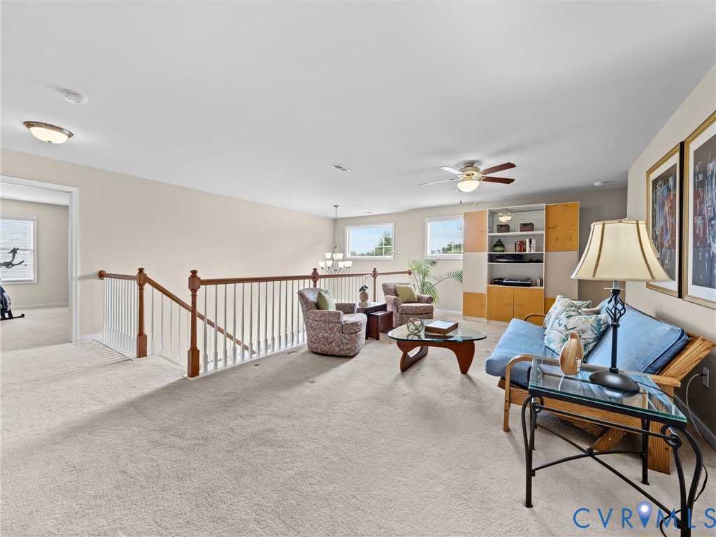 Spacious carpeted loft area with built-in shelving, a ceiling fan, and multiple windows