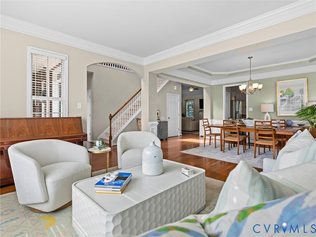 Hardwood flooring, crown molding, arched entryways, a tray ceiling, and a chandelier in the dining area