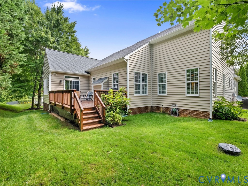 Exterior featuring light-colored siding, a wooden deck with railing, a shingled roof, a green lawn, and mature trees
