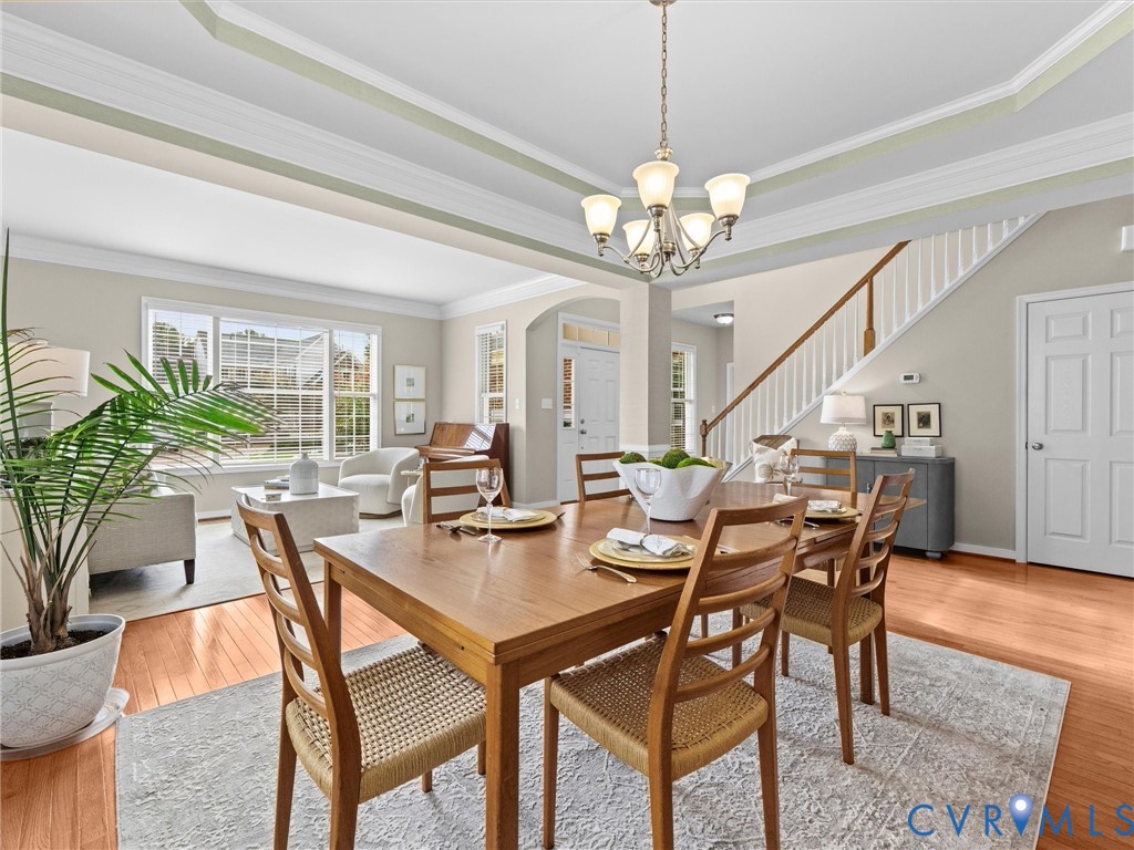 Tray ceiling with crown molding, chandelier lighting, wood-finish flooring, staircase with white spindles, and expansive windows