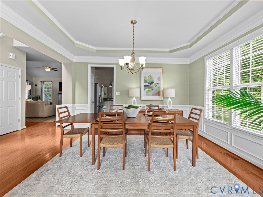 Hardwood flooring, tray ceiling, crown molding, double window, and a chandelier