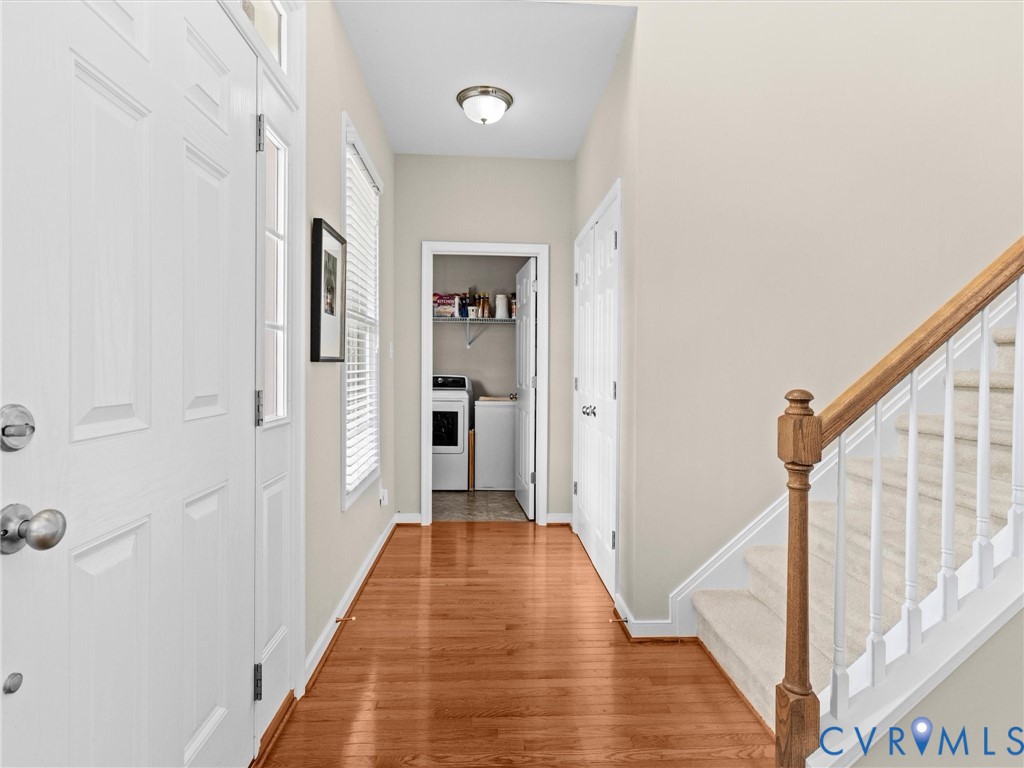 Hardwood-finish flooring extending through the entry, white paneled entry door with sidelight, and carpeted staircase with wood handrail and white balusters