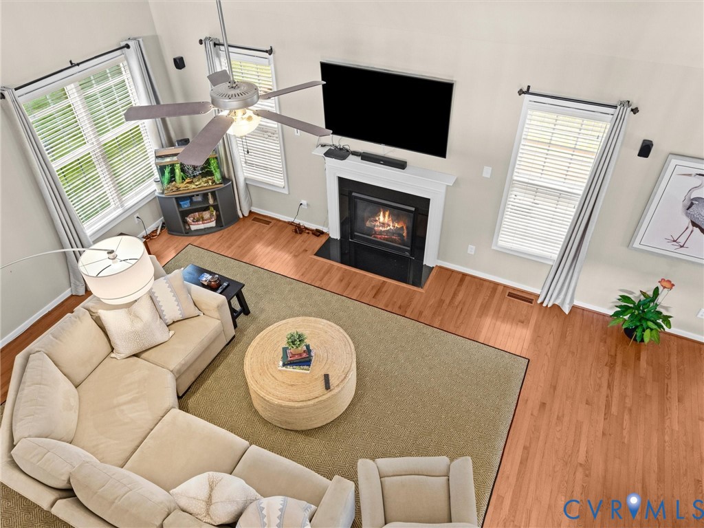 Vaulted ceilings, a built-in fireplace with a white mantel, hardwood flooring, and multiple windows with blinds