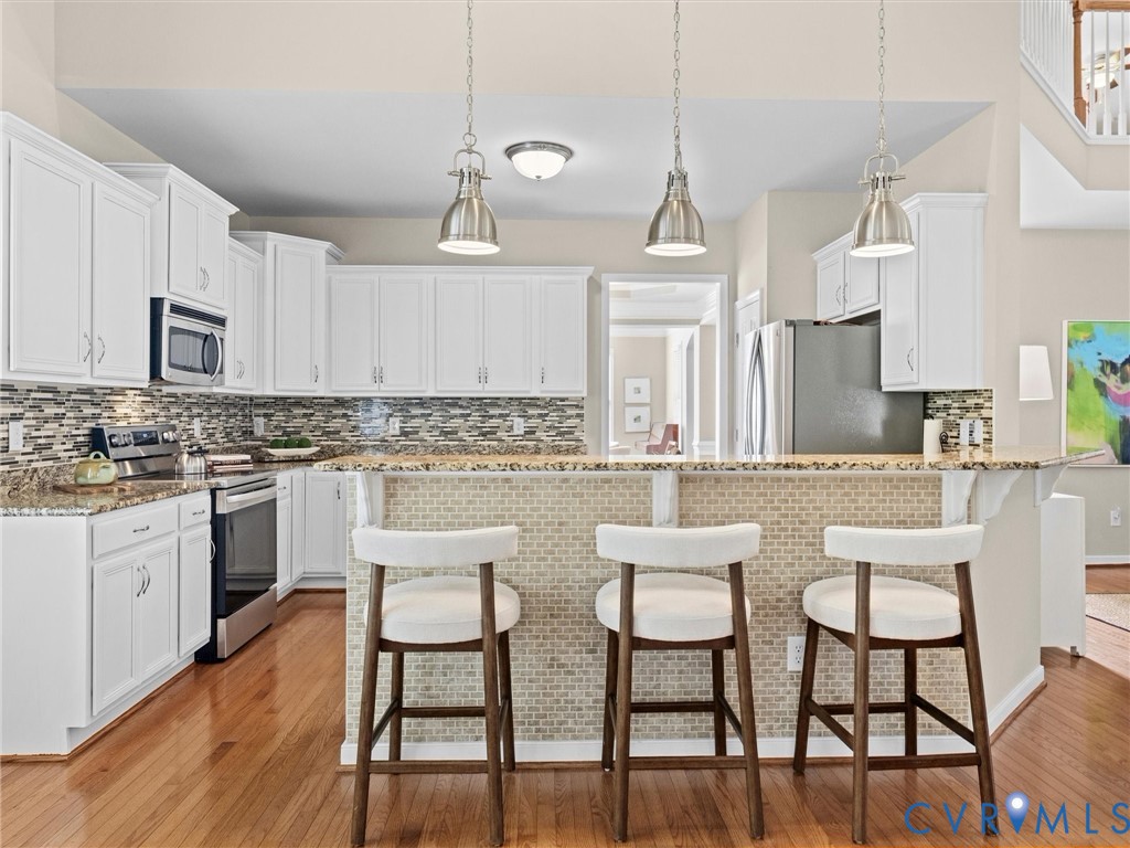 White cabinetry with stainless steel appliances, granite countertops, and a mosaic tile backsplash