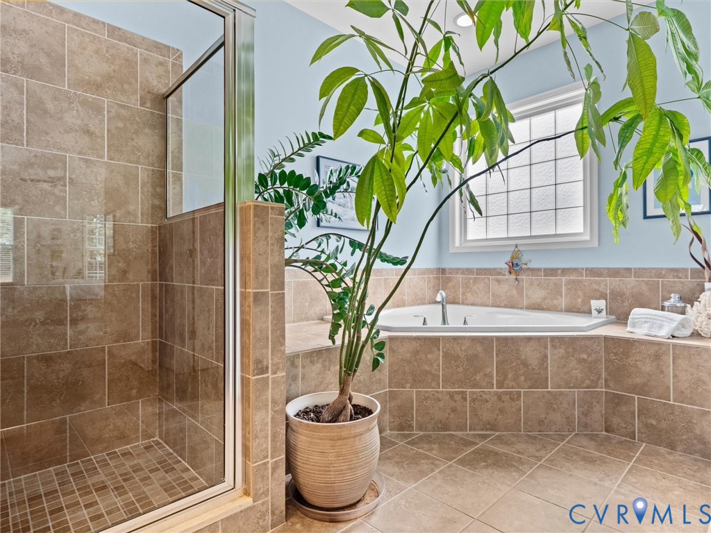 Tiled flooring with a corner soaking tub and an enclosed shower featuring a glass door