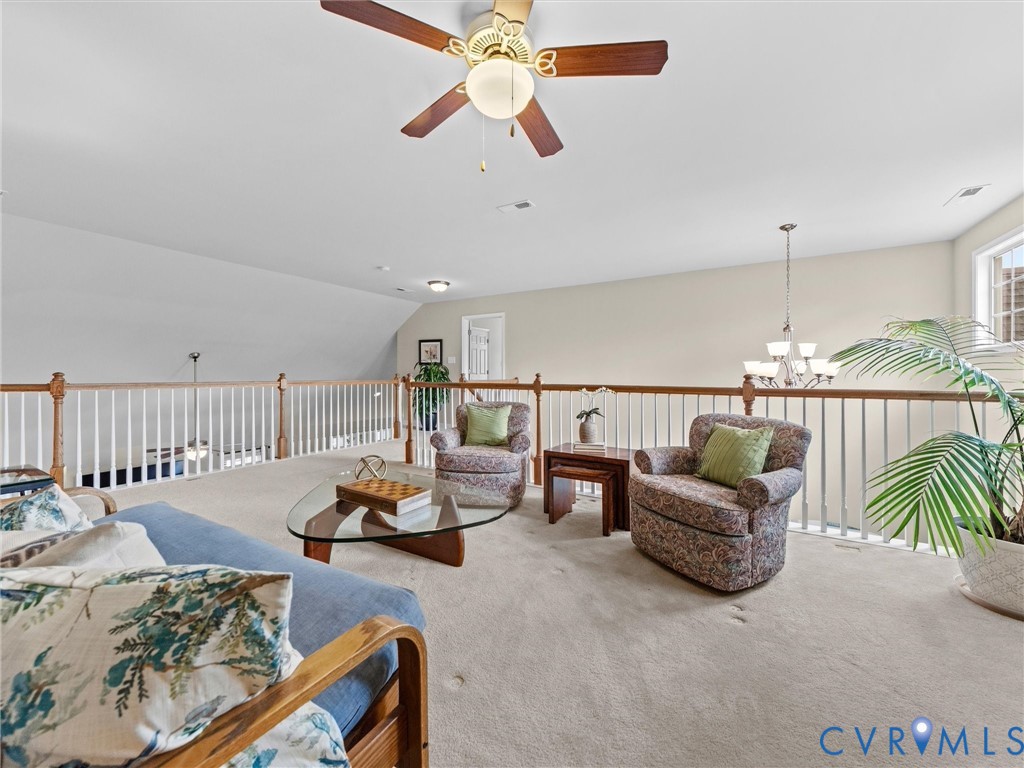 Carpeted loft area featuring a ceiling fan, white railing with wood-finish top rail, and a multi-light chandelier