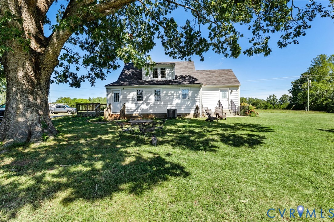 Expansive grassy yard with a mature shade tree, rear deck, and dormer windows on the white siding exterior