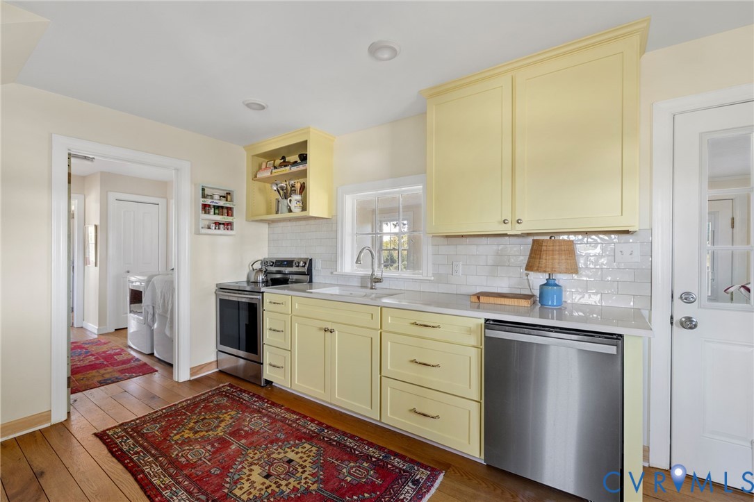 Kitchen featuring light yellow cabinetry, stainless steel appliances, a white subway tile backsplash, and wood-finish flooring