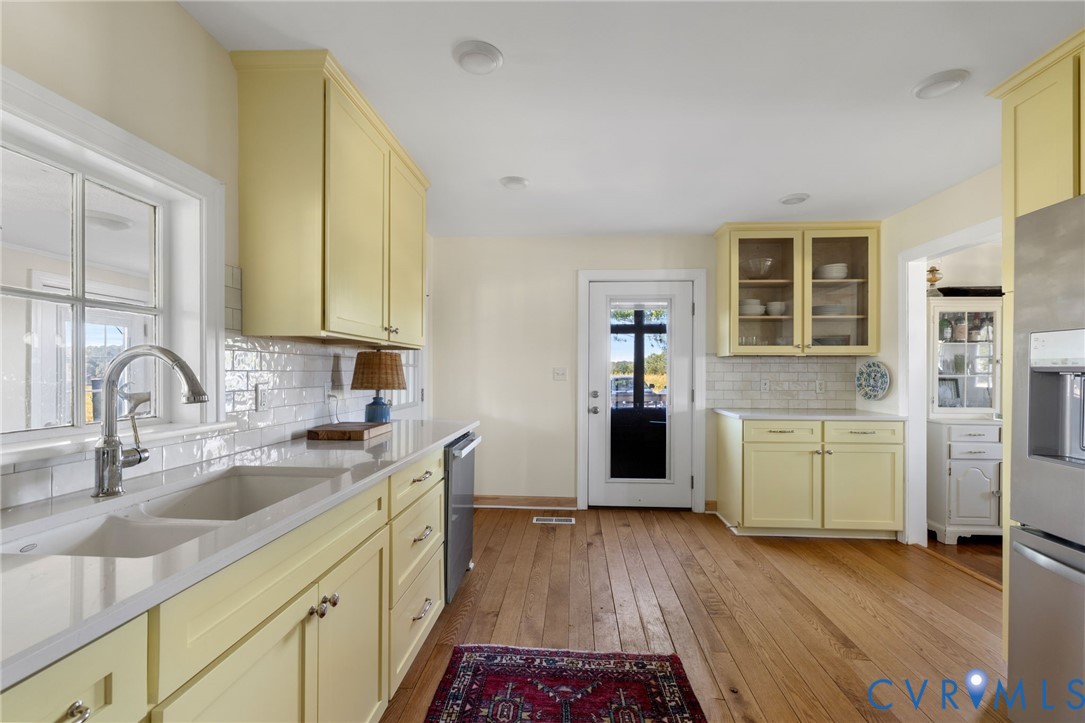 Kitchen featuring wood-finish flooring, light-toned cabinetry, subway tile backsplash, light-toned countertops, and a double basin sink