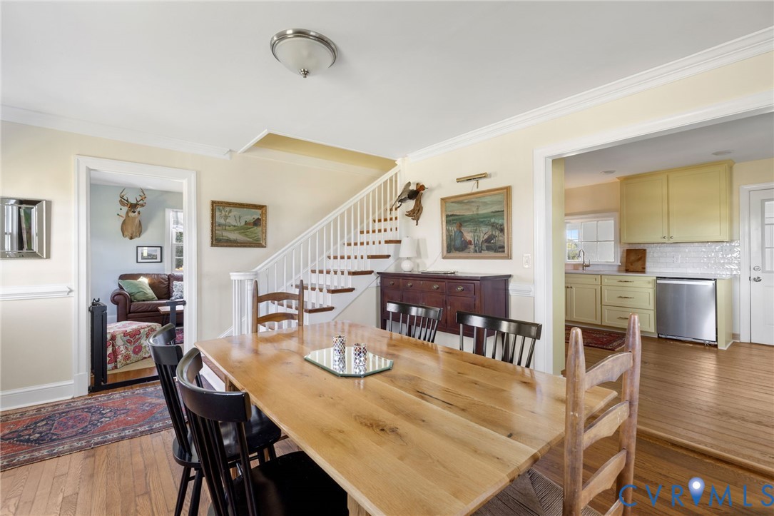 Dining area with wood-finish flooring, staircase with white risers, and crown molding